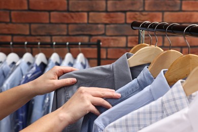 Dry-cleaning service. Woman taking shirt from rack against brick wall, closeup