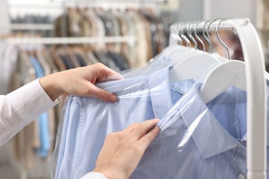 Photo of Dry-cleaning service. Woman taking shirt in plastic bag from rack indoors, closeup