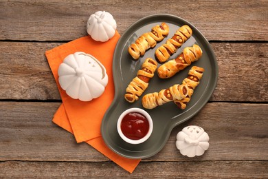 Photo of Cute sausage mummies served with ketchup on wooden table, flat lay. Halloween party food