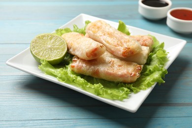 Photo of Delicious fried spring rolls on light blue wooden table