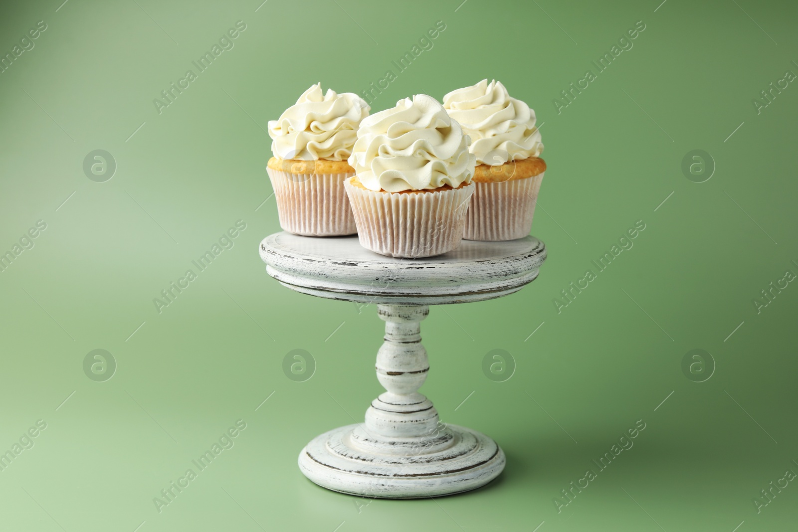 Photo of Tasty vanilla cupcakes with cream on green background