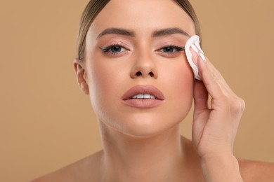 Photo of Beautiful woman removing makeup with cotton pad on beige background, closeup