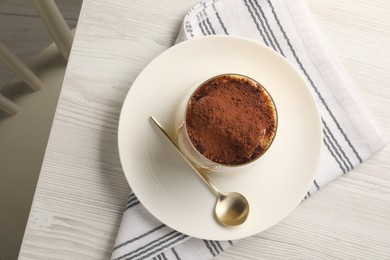 Photo of Delicious tiramisu in glass and spoon on white wooden table, top view