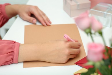 Photo of Young woman writing message in greeting card at white table, closeup