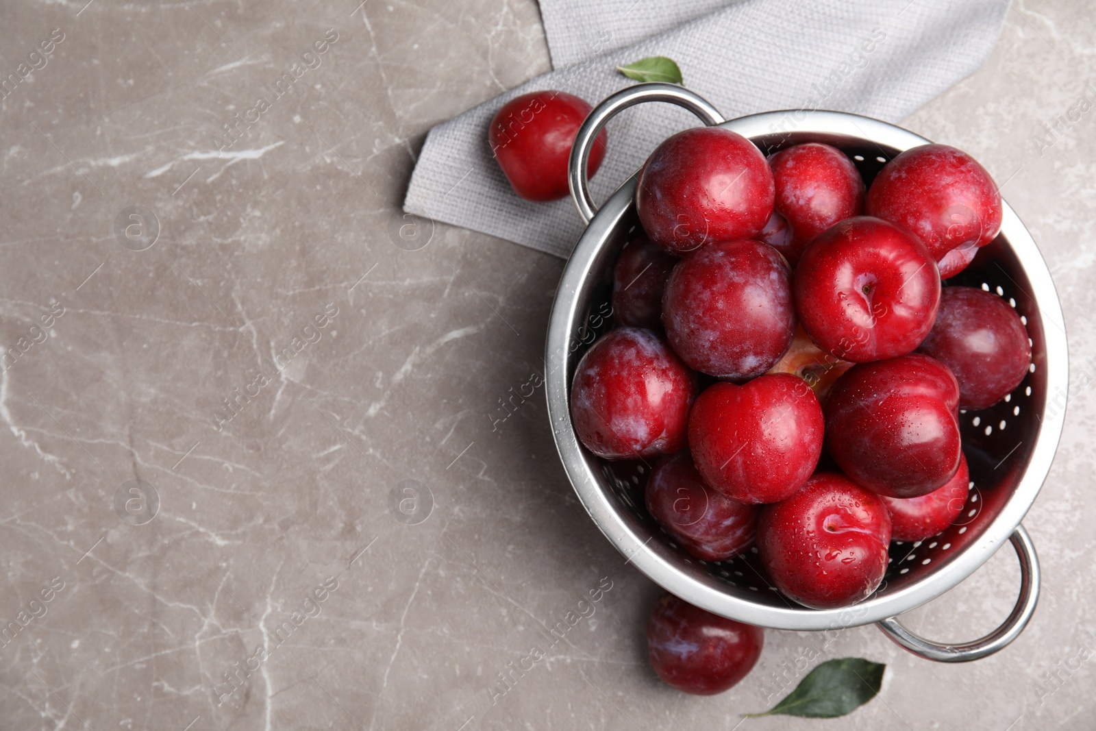 Photo of Delicious ripe plums in colander on grey marble table, flat lay. Space for text