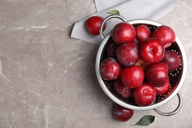 Photo of Delicious ripe plums in colander on grey marble table, flat lay. Space for text