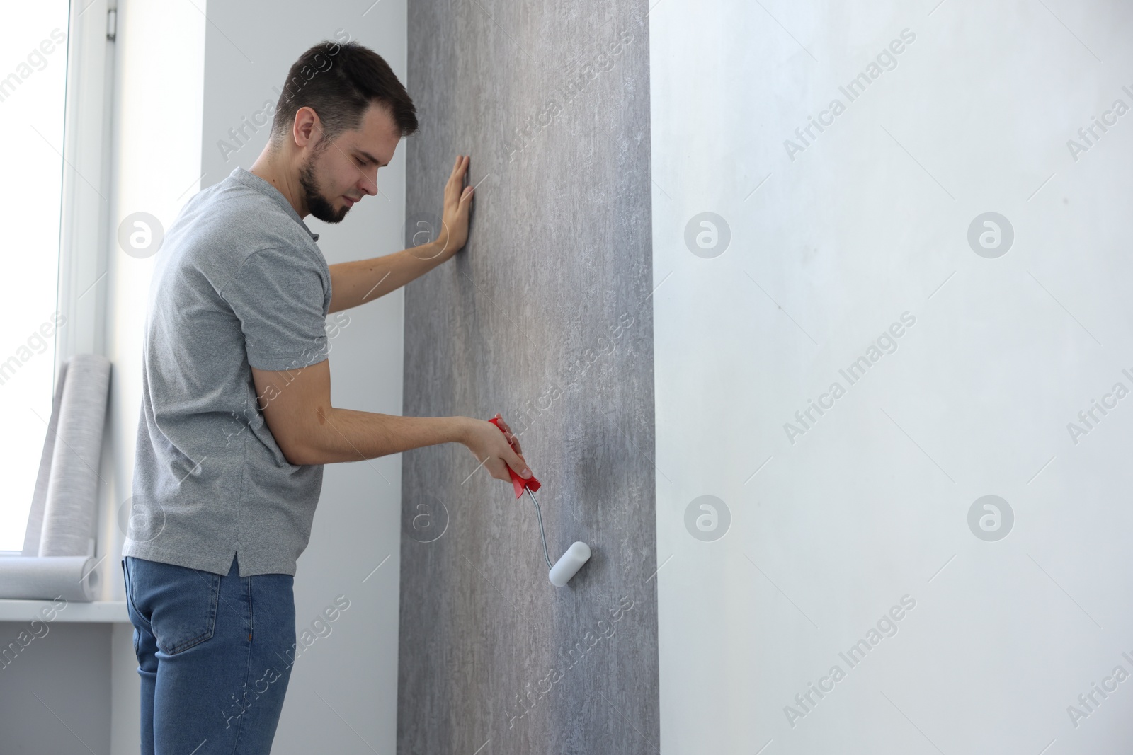 Photo of Man hanging stylish gray wallpaper in room