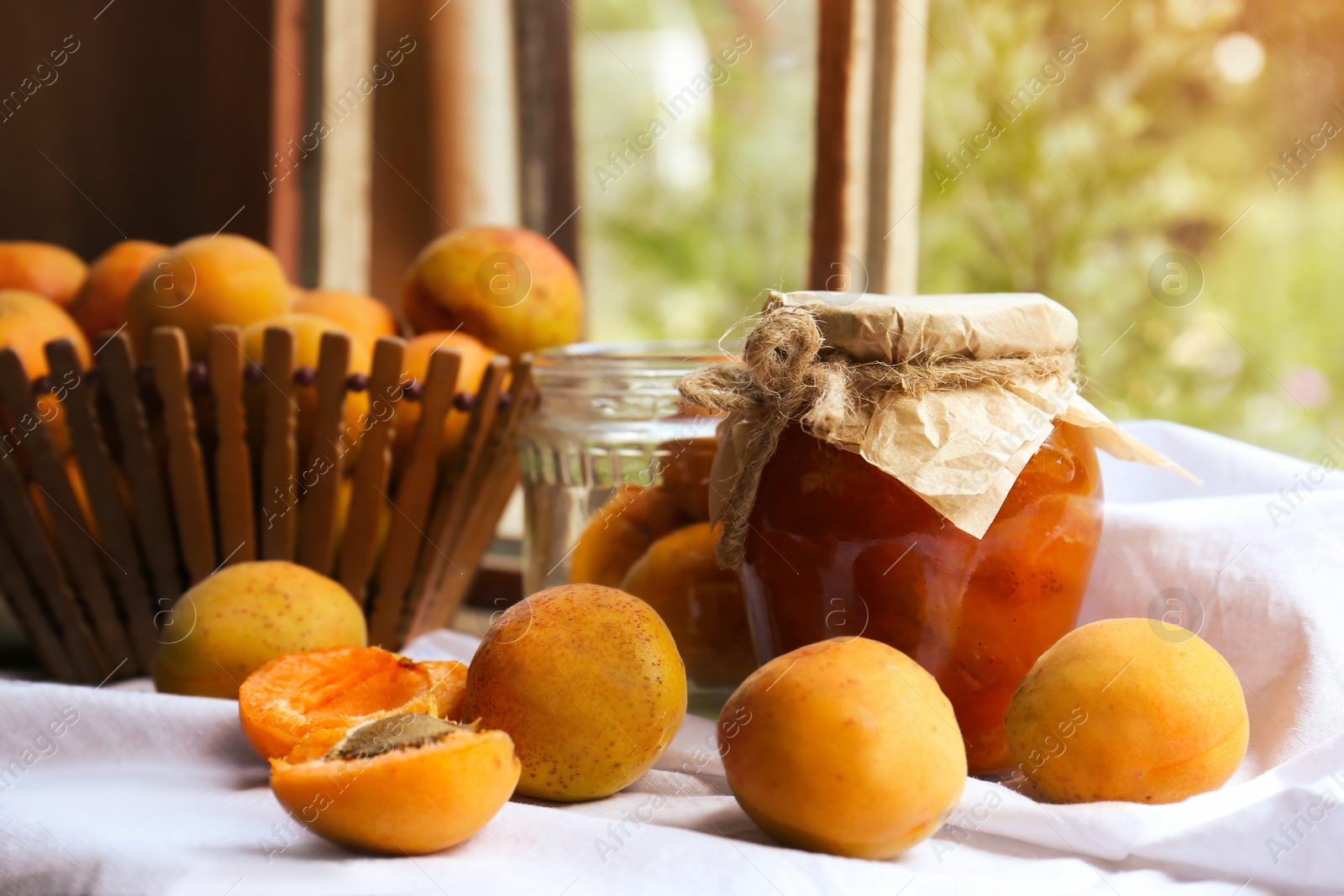 Photo of Jar of delicious jam and fresh ripe apricots on tablecloth indoors. Fruit preserve