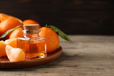 Photo of Bottle of tangerine essential oil and fresh fruits on wooden table, space for text
