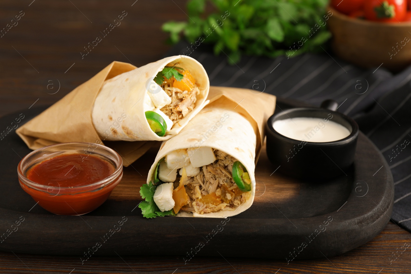 Photo of Delicious tortilla wraps with tuna, vegetables and sauces on wooden table