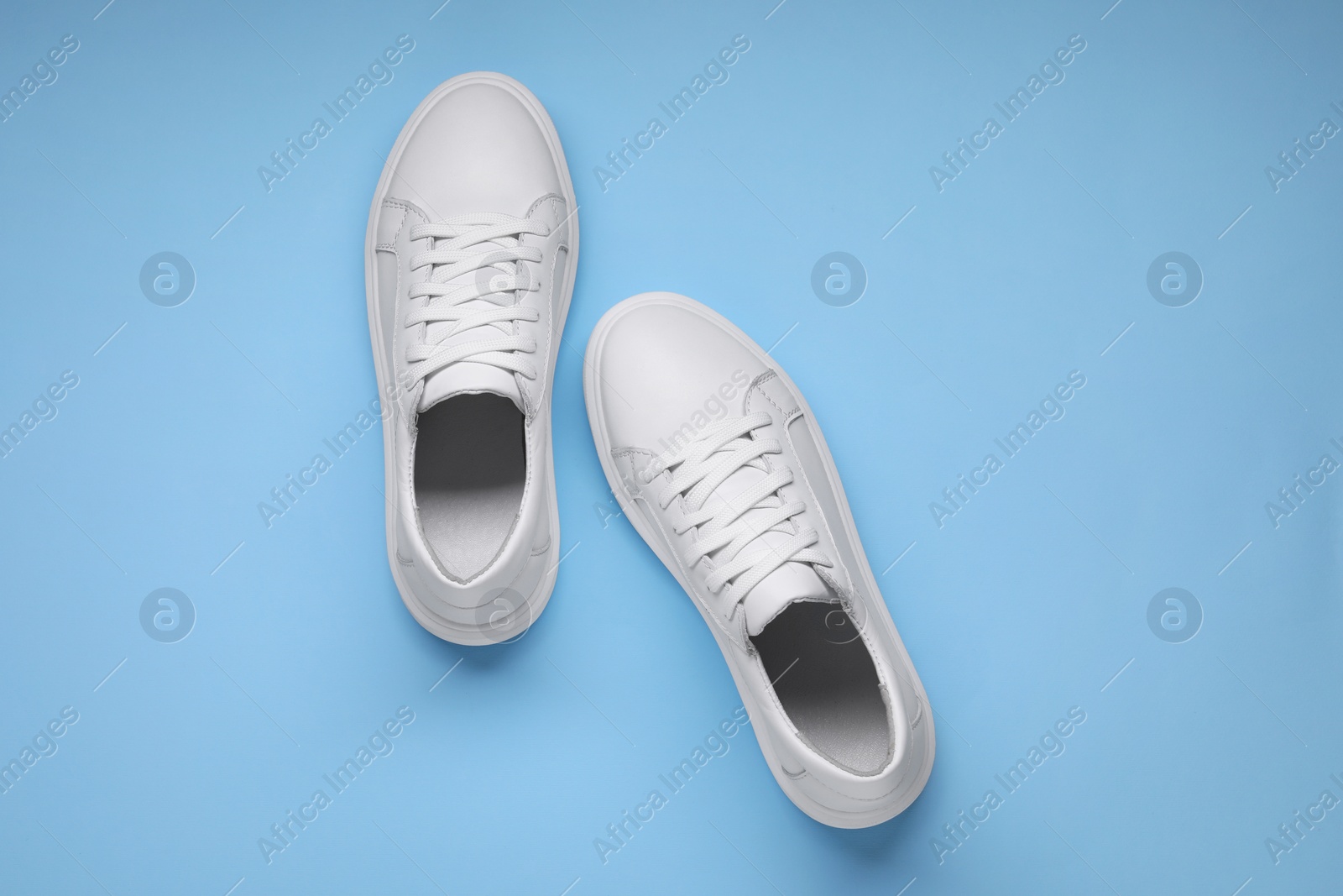 Photo of Pair of stylish white sneakers on light blue background, top view