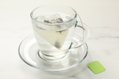 Photo of Tea bag in glass cup on white table, closeup