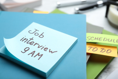 Photo of Reminder note about job interview and stationery on table, closeup