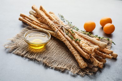 Photo of Delicious grissini sticks with oil, thyme and yellow tomatoes on grey table