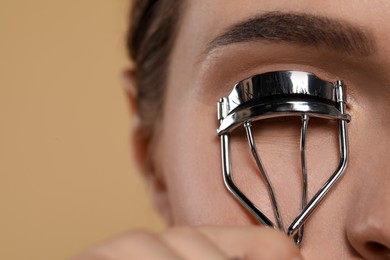 Woman using eyelash curler on beige background, closeup. Space for text