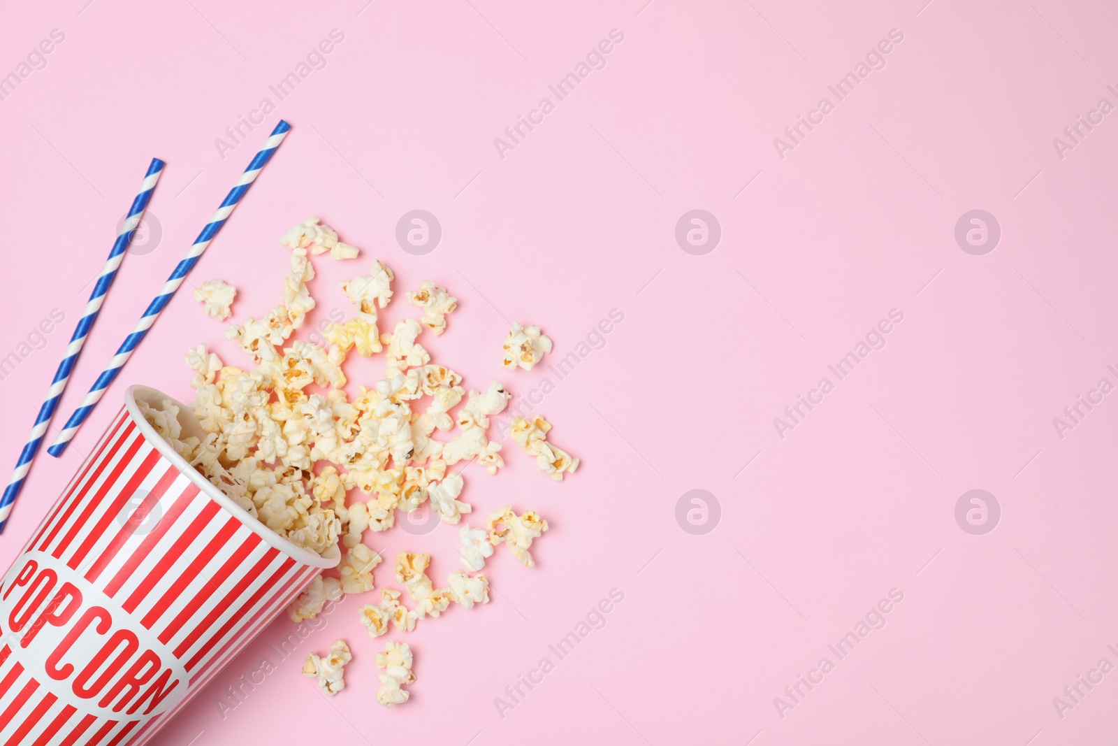 Photo of Overturned paper cup with tasty popcorn on color background, top view. Space for text