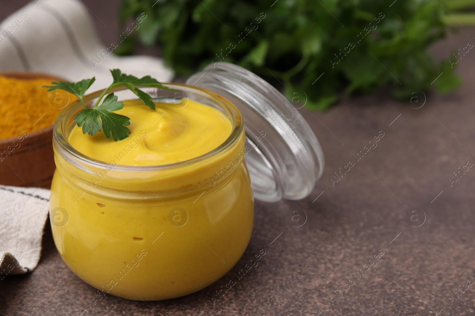 Photo of Jar with tasty curry sauce and parsley on brown table, closeup. Space for text