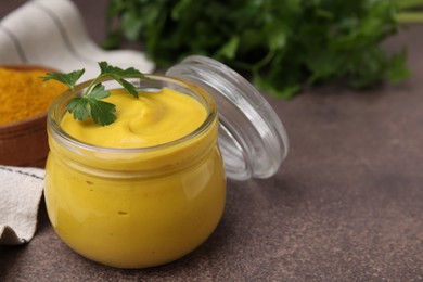 Photo of Jar with tasty curry sauce and parsley on brown table, closeup. Space for text