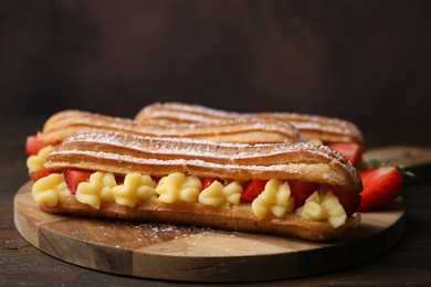 Photo of Delicious eclairs filled with cream and strawberries on wooden table