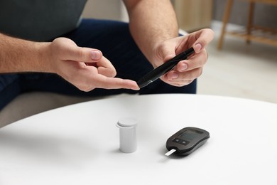 Photo of Diabetes test. Man checking blood sugar level with lancet pen at white table, closeup