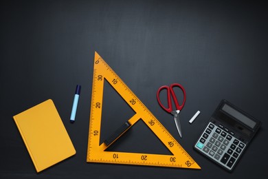Triangle ruler, scissors, chalk, calculator, marker and notebook on black table, flat lay