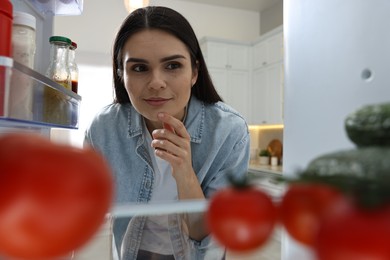 Photo of Thoughtful woman near refrigerator in kitchen, view from inside