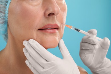 Doctor giving facial injection to senior woman on light blue background, closeup. Cosmetic surgery