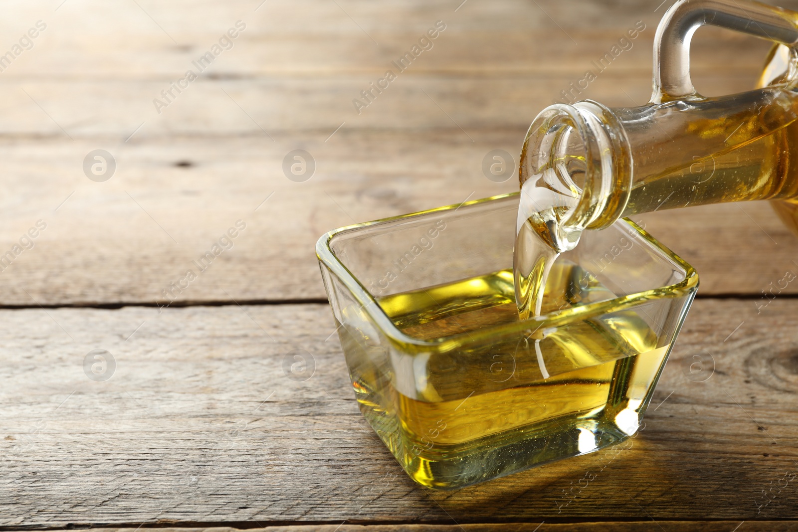 Photo of Pouring cooking oil from jug into bowl on wooden table. Space for text