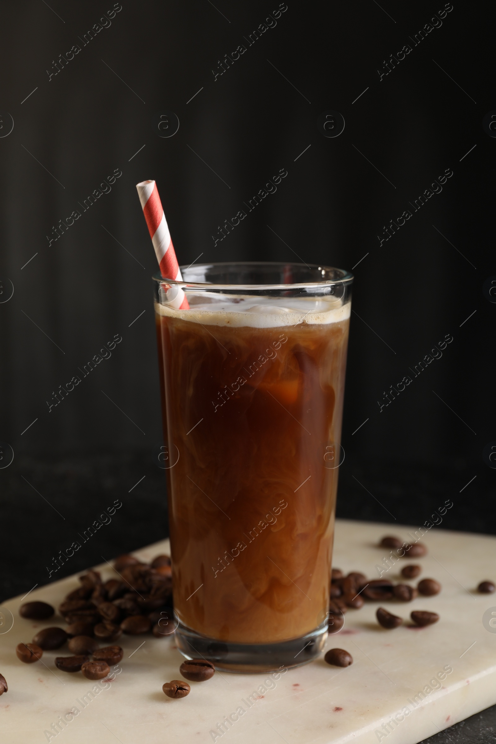 Photo of Refreshing iced coffee with milk in glass and beans on table against dark gray background