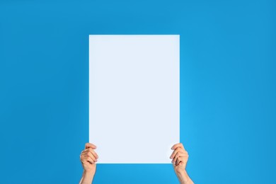 Man holding blank poster on blue background, closeup