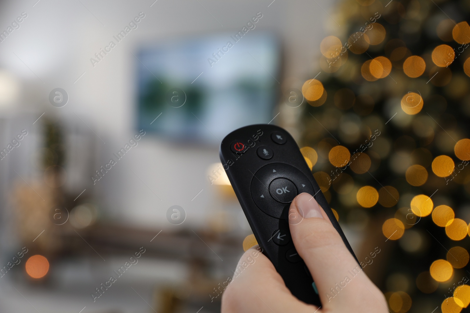 Photo of Woman with remote control in room decorated for Christmas, closeup