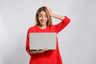 Portrait of emotional woman with modern laptop on light grey background