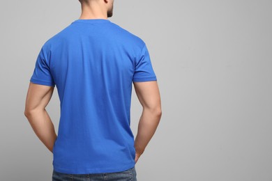 Man wearing blue t-shirt on light grey background, back view. Mockup for design