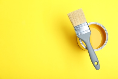 Paint can and brush on yellow background, top view. Space for text