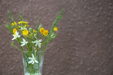 Bouquet of beautiful wildflowers in glass vase near brown wall, closeup. Space for text