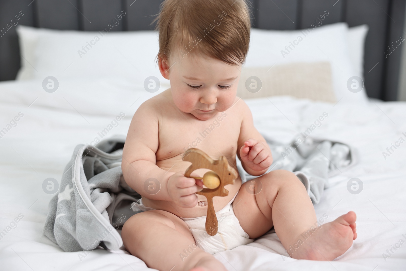 Photo of Cute baby boy with blanket and rattle sitting on bed at home