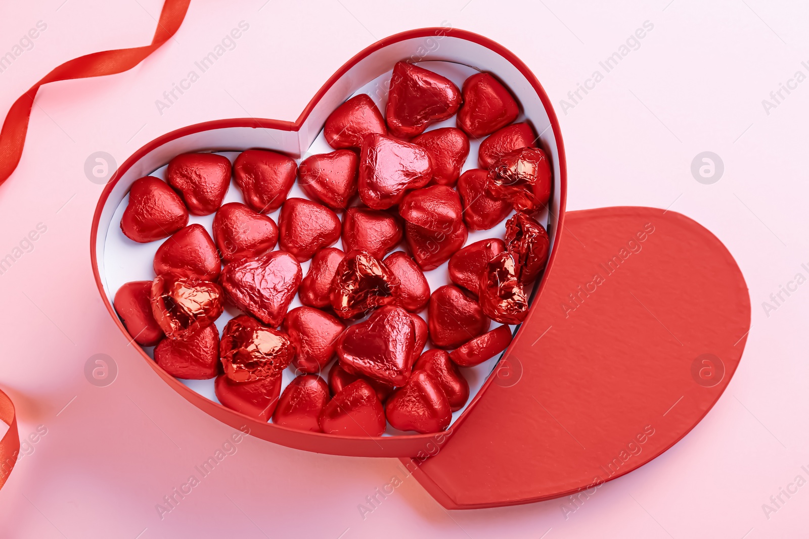 Photo of Box of heart shaped chocolate candies and ribbon on pink background, flat lay