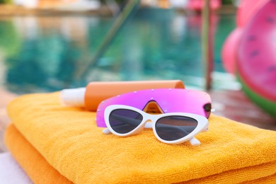 Beach towels, sunglasses and sunscreen on sunbed near outdoor swimming pool, closeup. Luxury resort