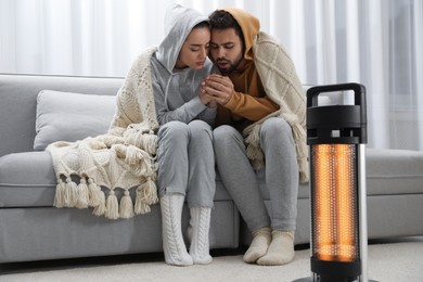 Photo of Young couple getting warm near electric heater at home