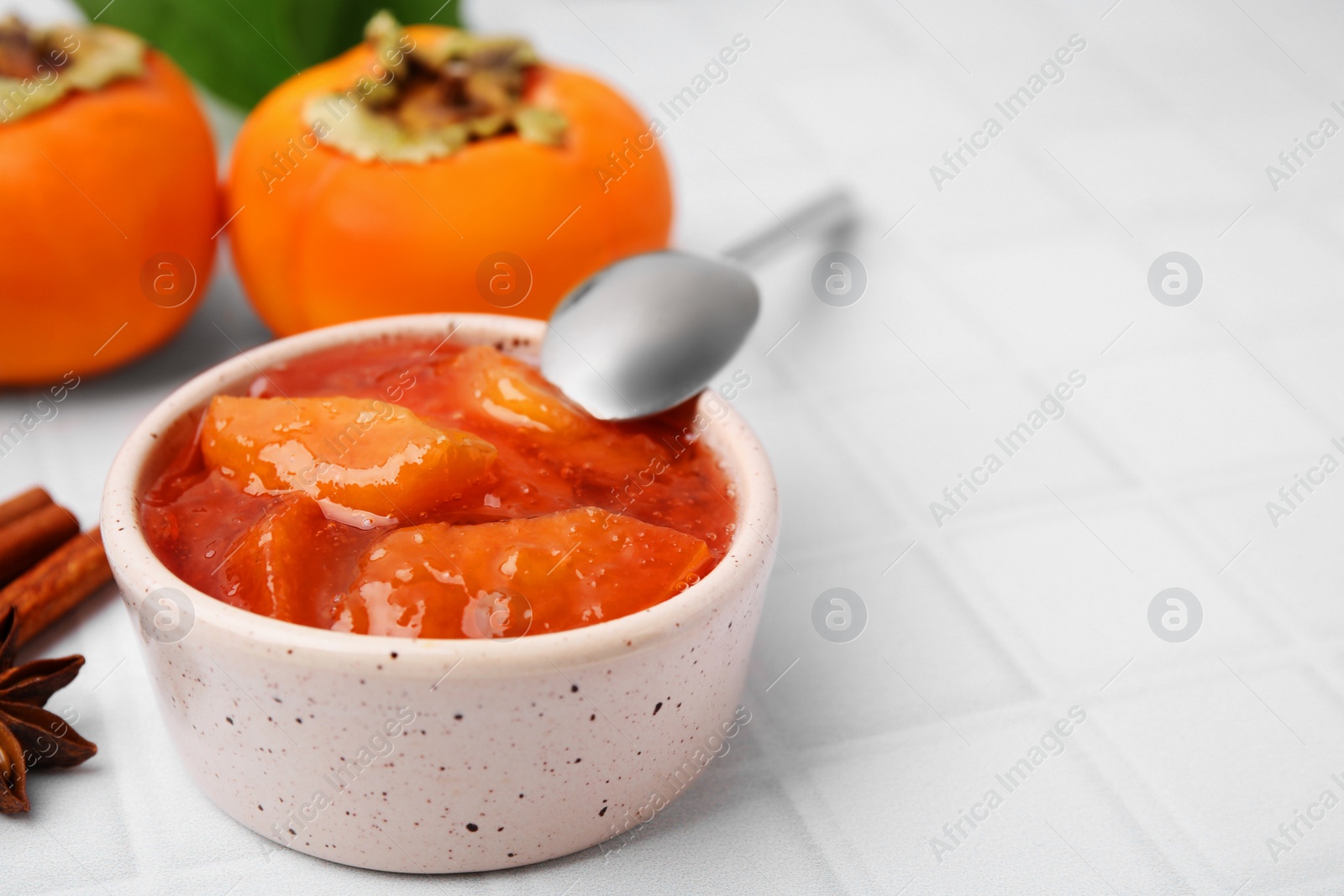 Photo of Bowl of tasty persimmon jam and ingredients on white tiled table. Space for text