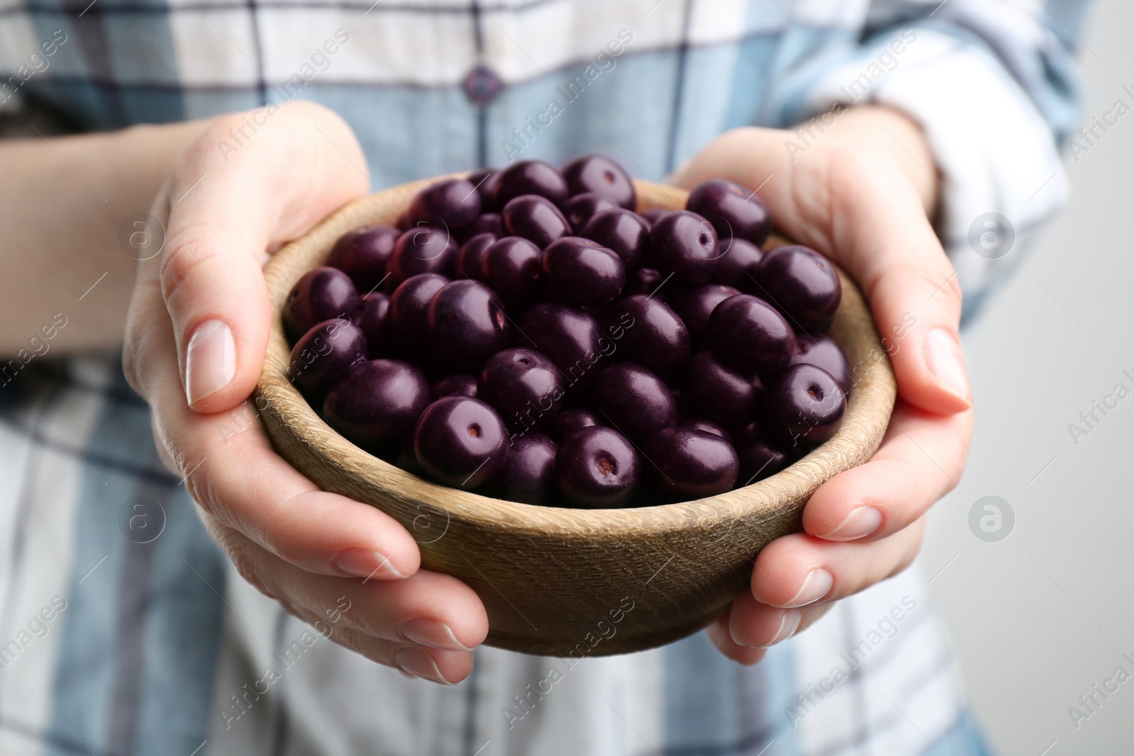 Photo of Woman holding tasty acai berries on light background, closeup