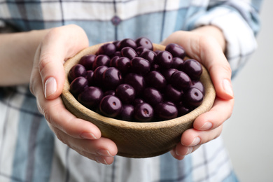 Woman holding tasty acai berries on light background, closeup