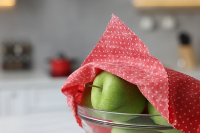 Apples in bowl covered with beeswax food wrap against blurred background, closeup. Space for text