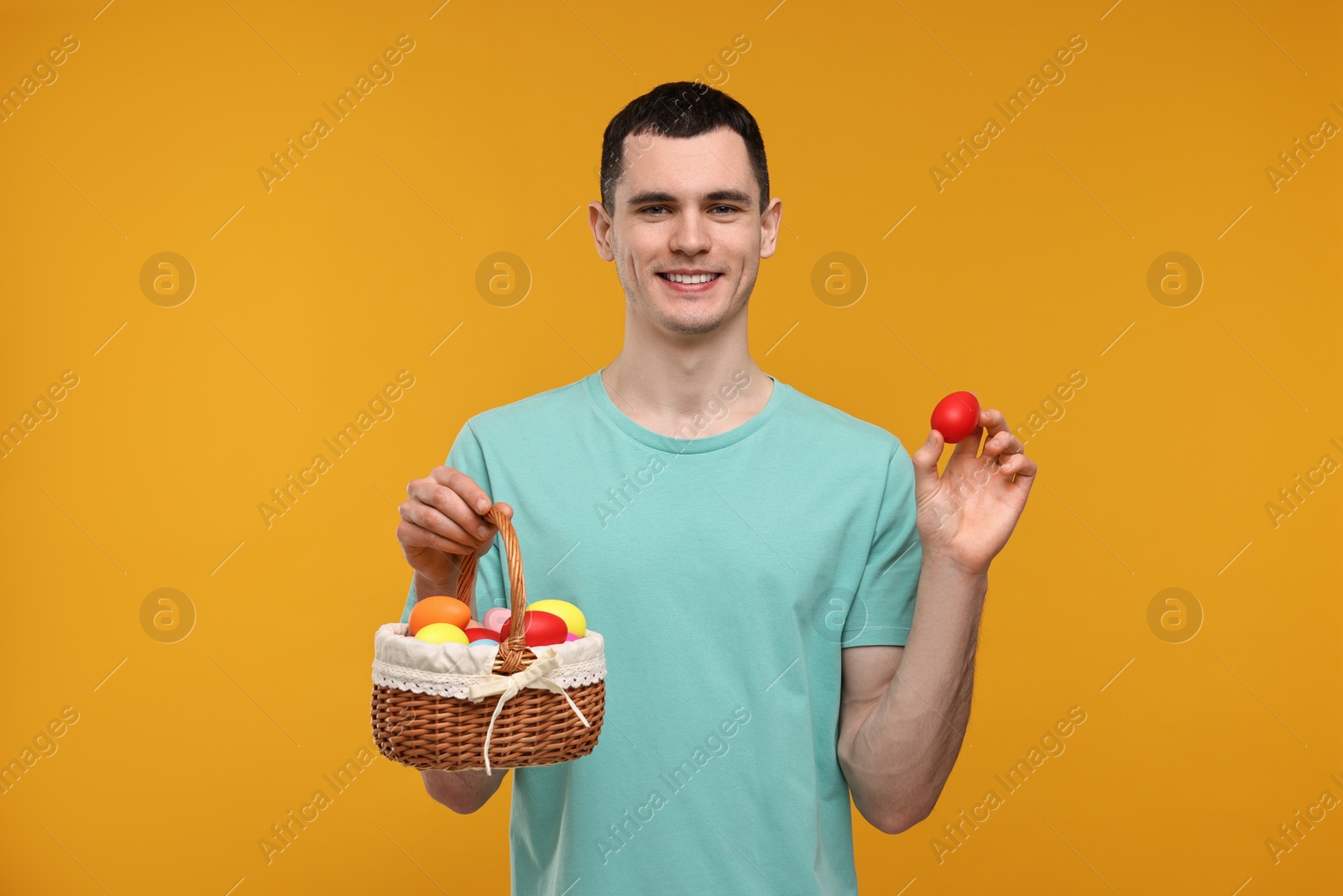 Photo of Easter celebration. Handsome young man with painted eggs on orange background