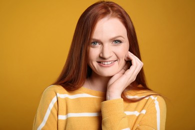 Candid portrait of happy young woman with charming smile and gorgeous red hair on yellow background