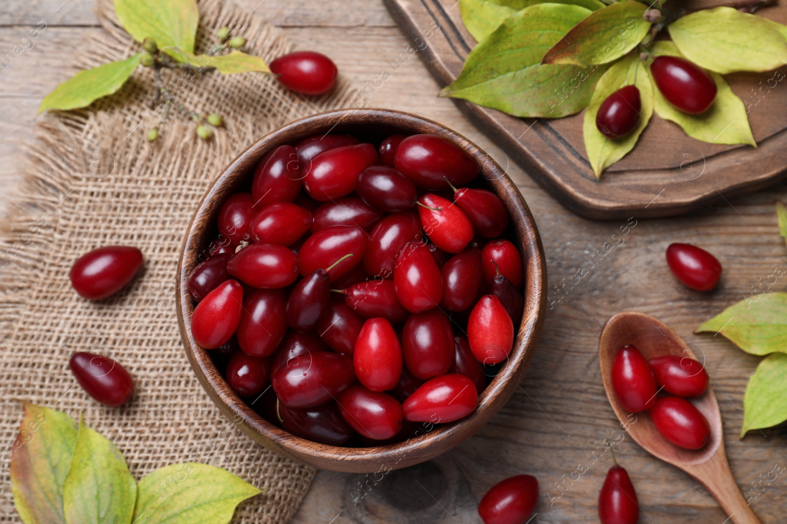 Photo of Fresh ripe dogwood berries with green leaves on wooden table, flat lay