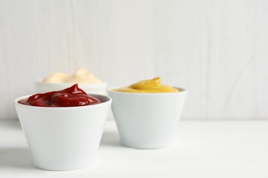 Photo of Ketchup, mustard and mayonnaise in bowls on white table, space for text