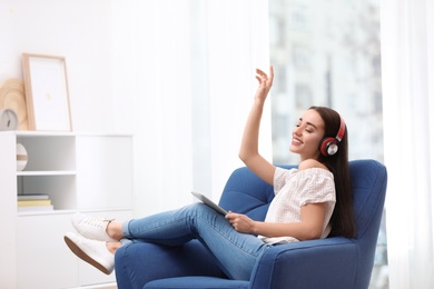 Photo of Young woman with headphones and tablet sitting in armchair at home
