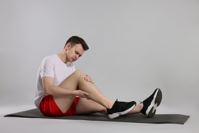 Man suffering from leg pain on mat against grey background