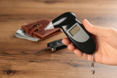 Photo of Woman holding modern breathalyzer with blank screen at wooden table, closeup